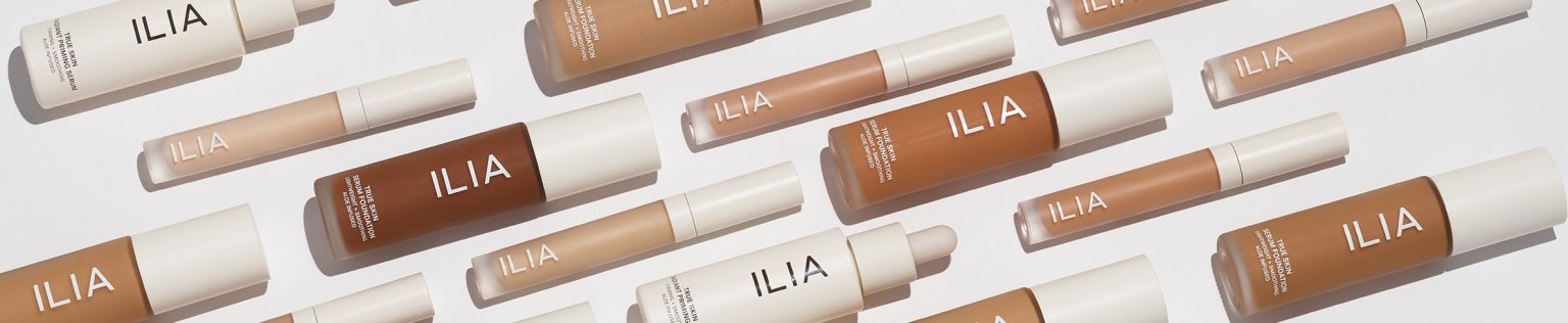 A variety of ILIA Complexion products, including foundations and concealers, displayed diagonally.